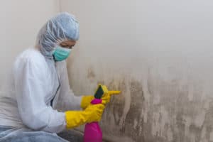 A person in white suit and yellow gloves spraying on the wall.